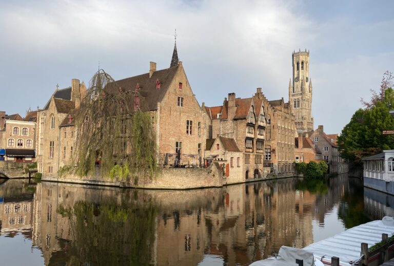 Old buildings reflecting in smooth canal water in Bruges Belgium