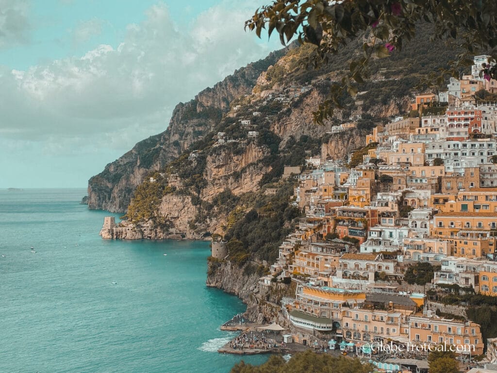 View of buildings in Positano Italy built up the side of a steep hill with the ocean in front.