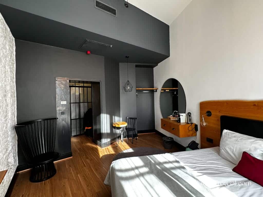 Hotel room with a gray back wall and white side walls, wooden floor, black chairs, and bed at the Hotel Rum in Budapest Hungary