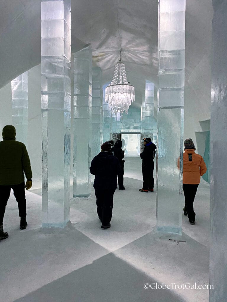 Inside the entrance of the the Icehotel in Jukkasjärvi, Sweden with people walking in between ice pillars supporting the ice ceiling.