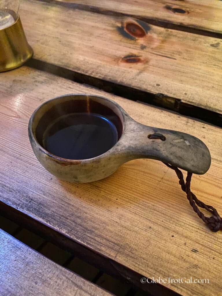 A wooden Sami kuksa cup filled with coffee sitting on a wooden slatted table