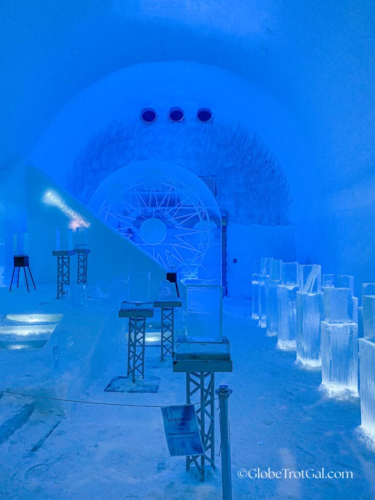 Room with intricately carved ice walls and six metal stands with clear ice blocks on them in the Ice Bar at the Icehotel in Jukkasjärvi, Sweden