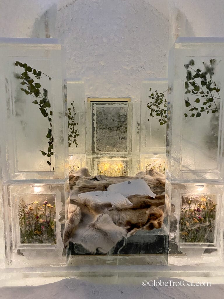 Room made with blocks of ice and a bed frame made of ice with a mattress and animal hides on it at the Icehotel in Jukkasjärvi, Sweden