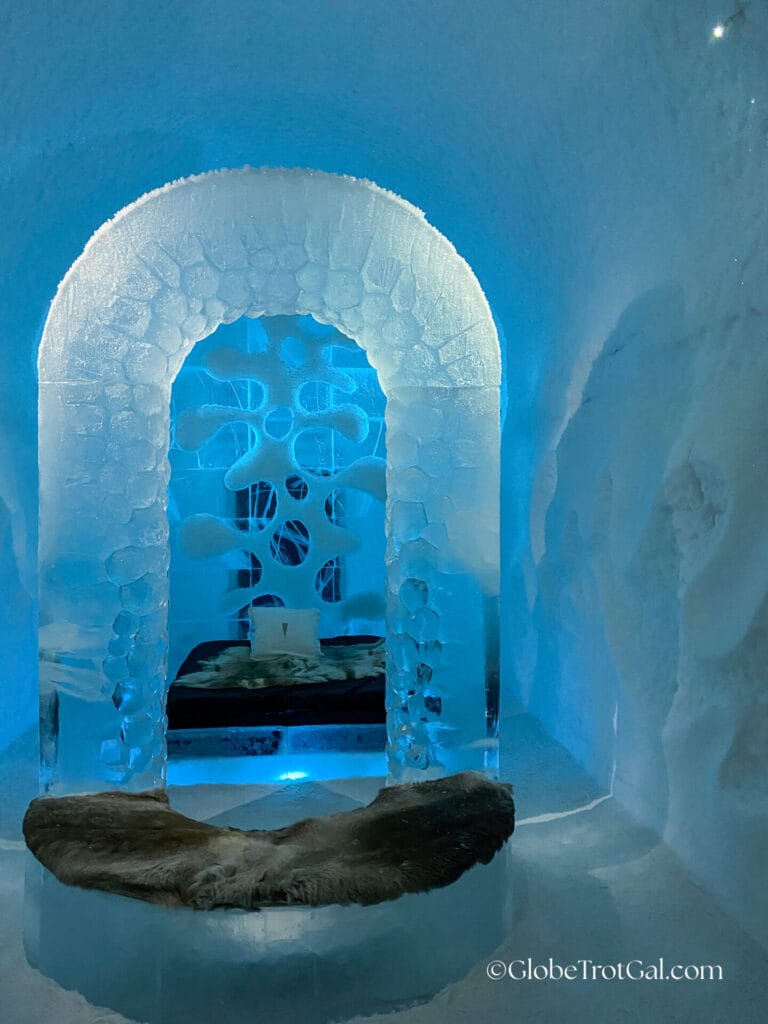 Textured arch carved of ice with a rounded bench in front covered with reindeer hide at the Icehotel in Jukkasjärvi, Sweden