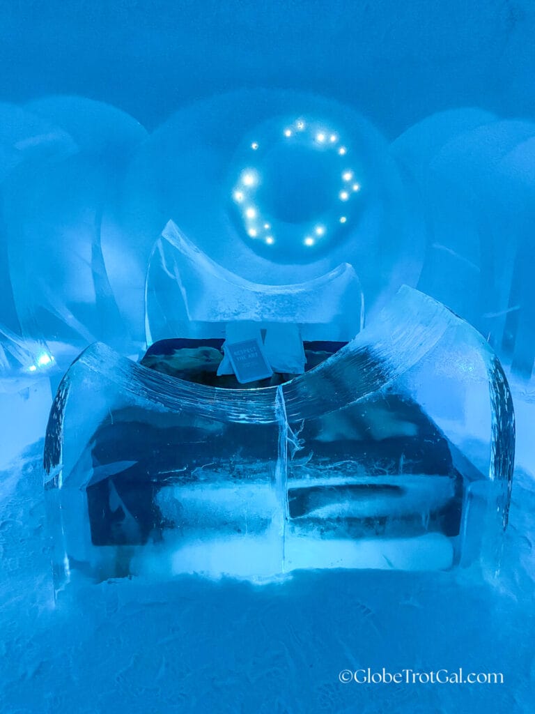 Bed with a curved frame made of clear ice glowing blue at the Icehotel in Jukkasjärvi, Sweden