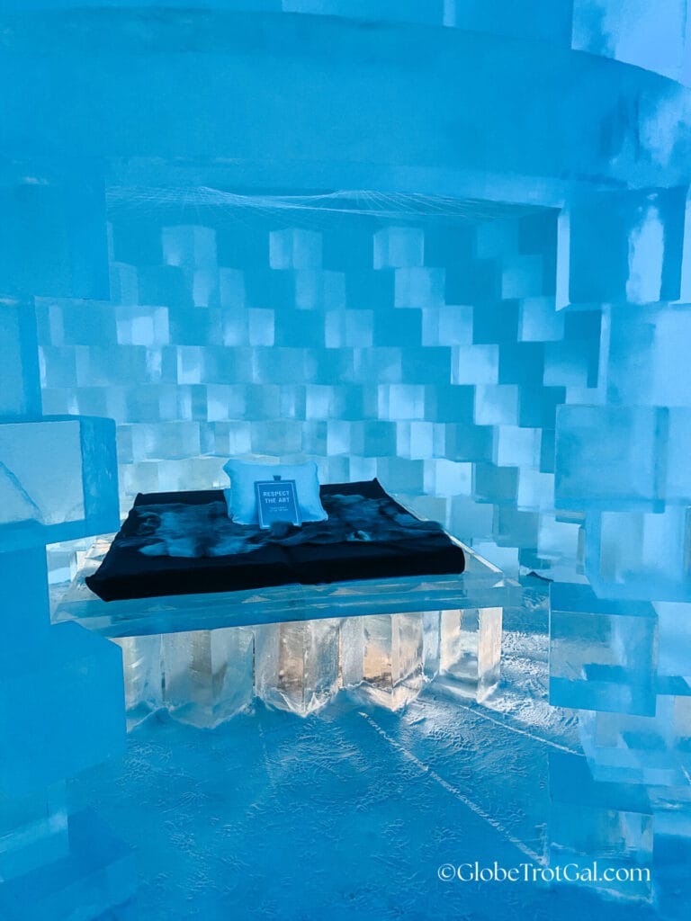 Art suite ice room with glowing blue blocks of ice and a bed with animal hides on it at the Icehotel in Jukkasjärvi, Sweden