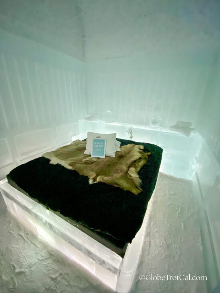 A bed frame made of ice with a mattress covered in reindeer hides surrounded by carved walls made of ice at the Icehotel in Jukkasjärvi, Sweden