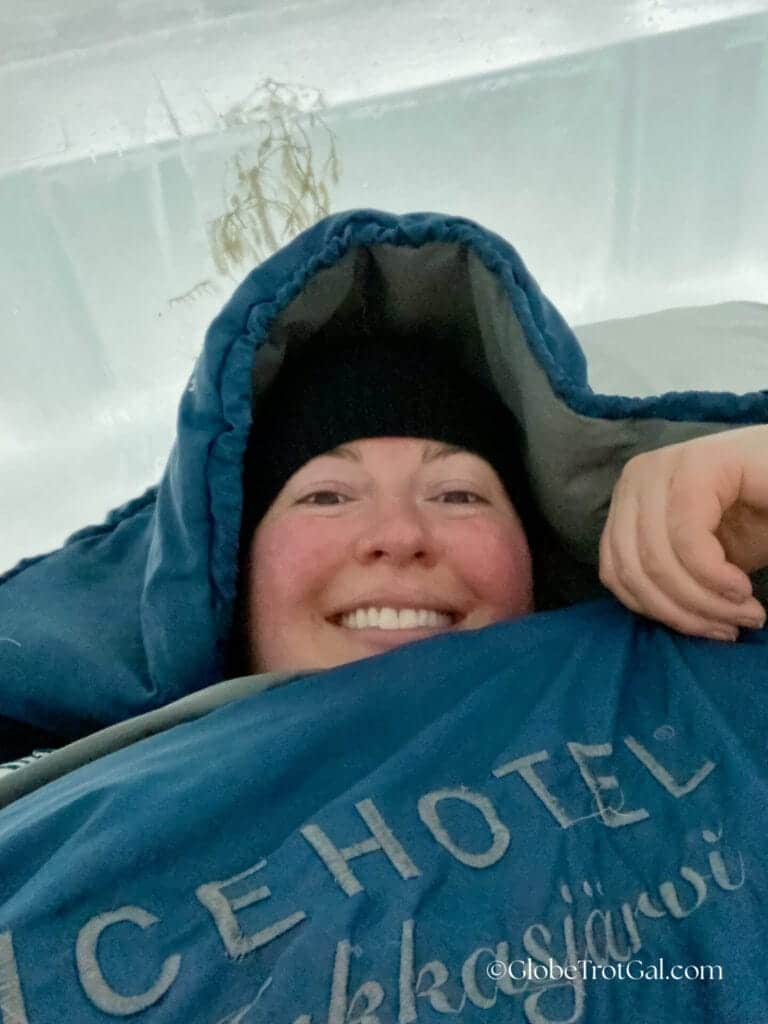 The author in a sleeping bag with the Icehotel logo sewn onto the front laying down on the ice bed at the Icehotel in Jukkasjärvi, Sweden