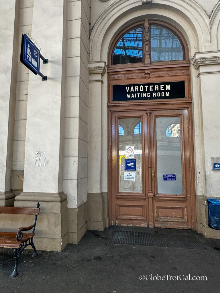 Wooden double doors to Budapest Keleti Station First Class Lounge with a black sign above them saying "Waiting Room" in English and Hungarian.