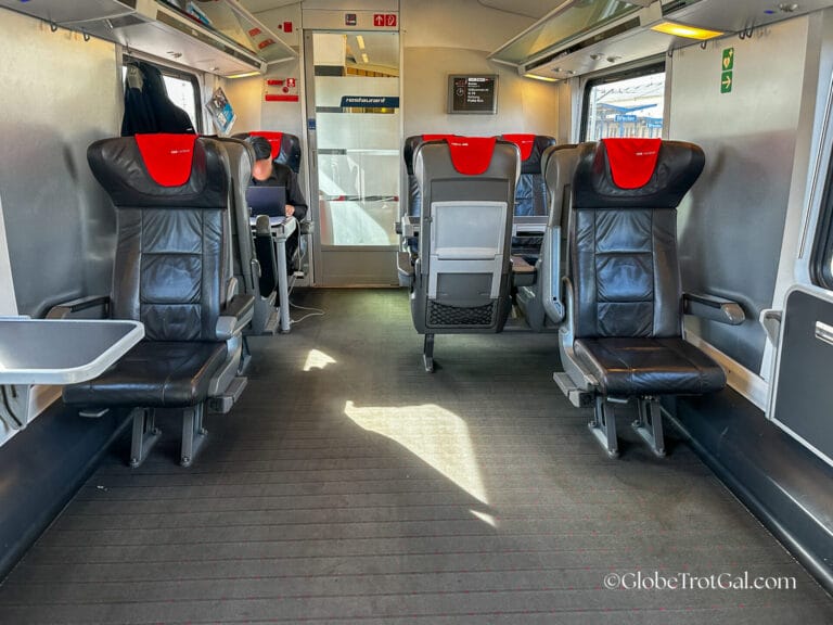 First class train car on OBB Railjet train with black leather train seats with red headrests.
