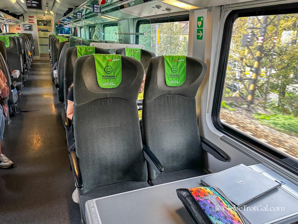 Economy class gray velour double seat with green headrest facing a table in an OBB Railjet train quiet car.