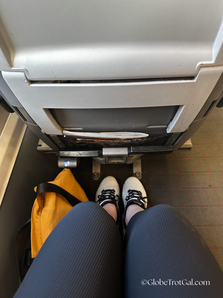 Person sitting in train seat wearing black stretchy pants and white sneakers taking a picture of leg room in OBB Railjet first class seat.