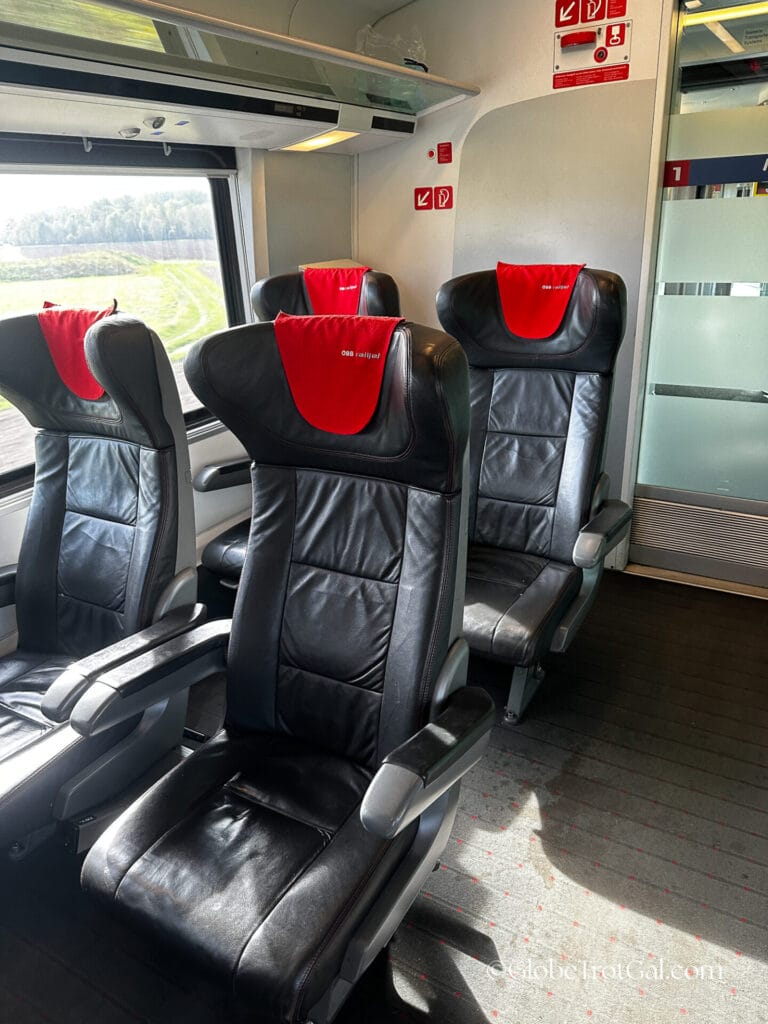 Four OBB Railjet black leather first class seats with red headrests in an OBB Railjet first class train car.