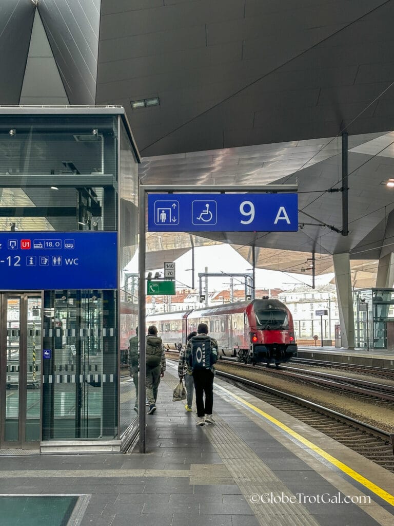 View down the track on Platform 9 at Vienna Central Train station with a red train approaching the opposite platform.
