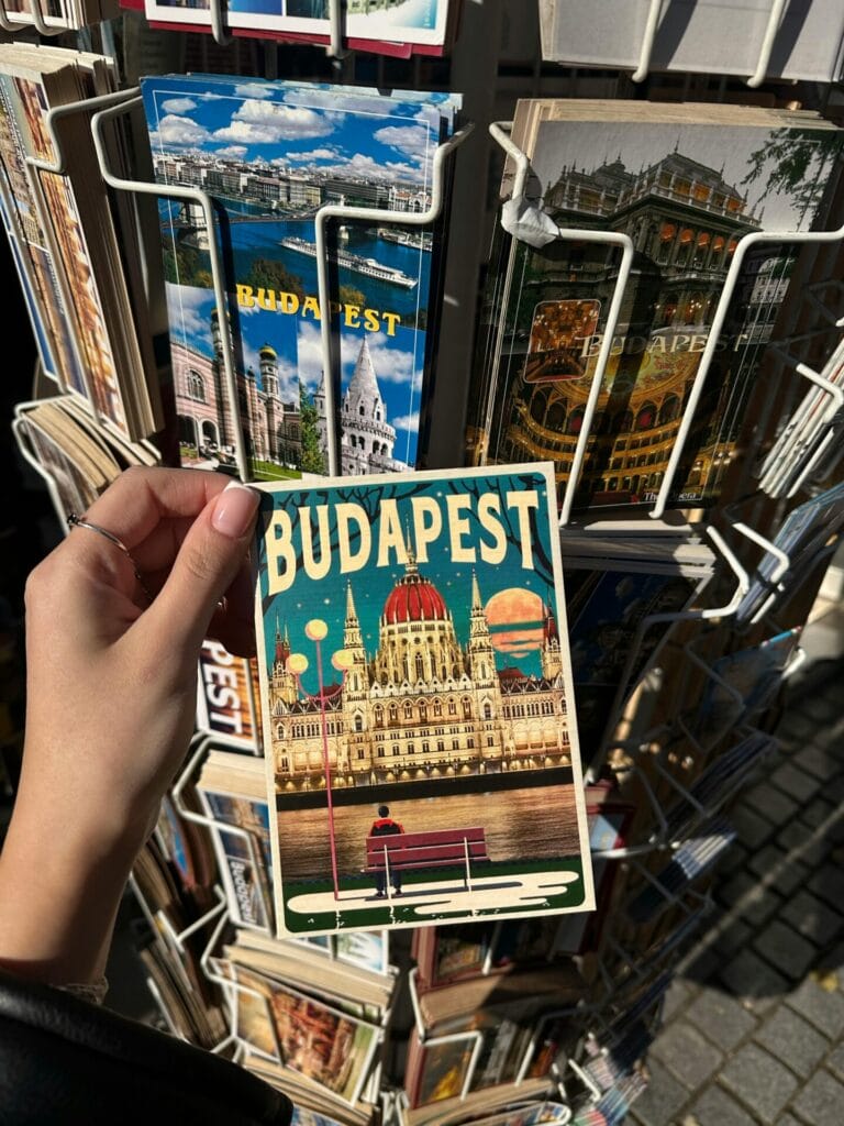 hand holding vintage Budapest postcard in front of a store display of postcards