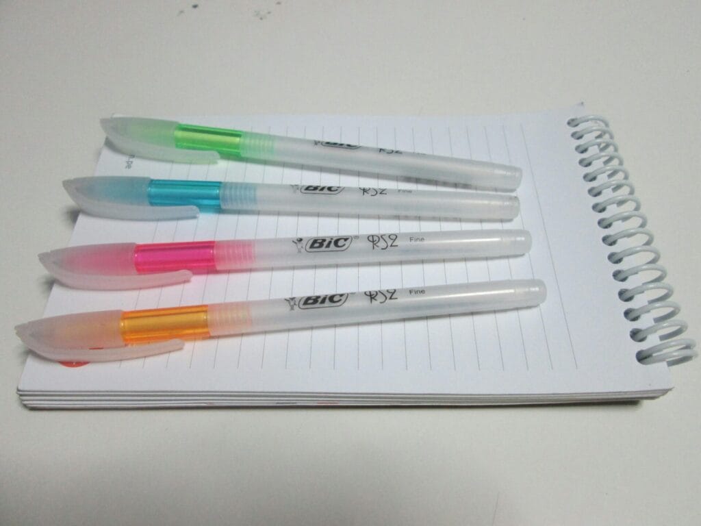 four Bic fine point pens in bright colors sitting on top of an open notepad