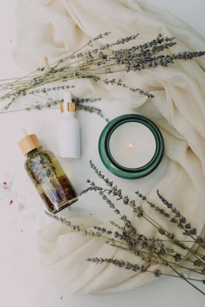 Dried lavender sprigs surrounding a candle and a bottle of lavender oil