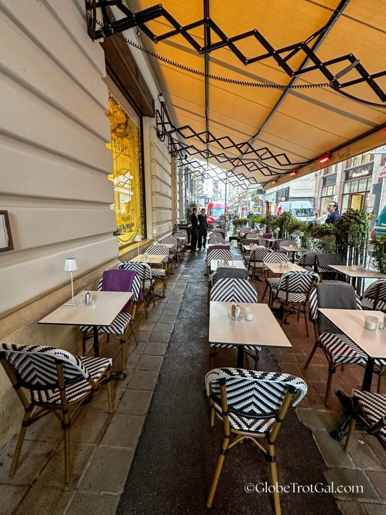 Outdoor cafe tables under a yellow awning at Cafe Demel in Wien, Austria