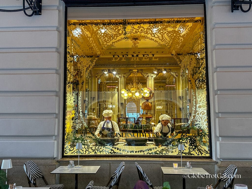 Large window with gold lettering and designs showcasing chefs making Kaiserschmarrn at Cafe Demel in Wien Austria