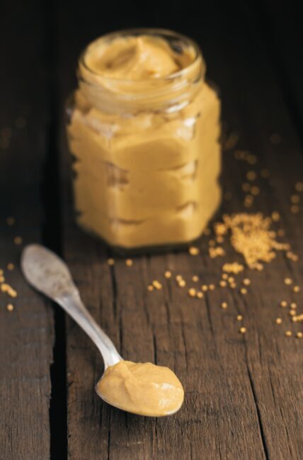 Jar of yellow mustard on a table with a spoon next to it