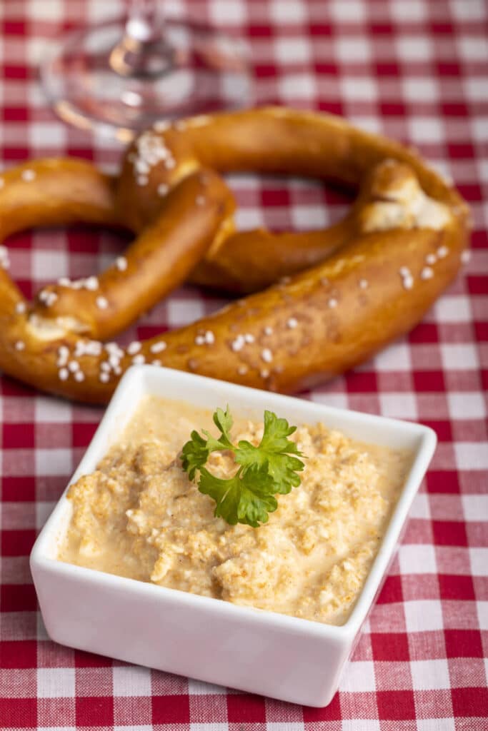 Closeup image of soft pretzel and obatzda beer cheese in a dish on a red checkered tablecloth